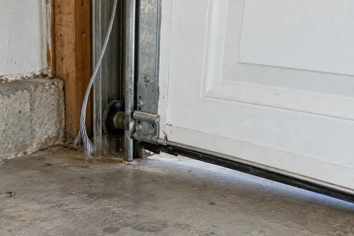 Snapped lift cable hanging by the bottom corner of a garage door