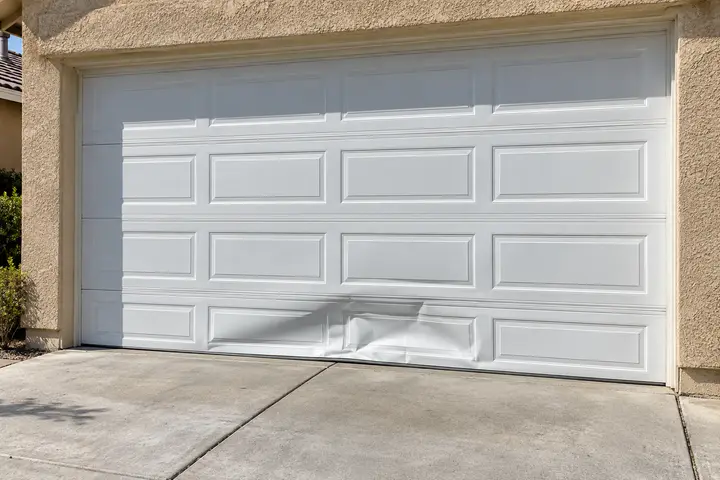 Dented bottom panel of a white garage door